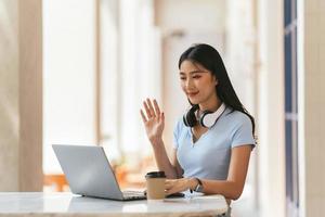 mulher asiática tendo chamada de vídeo em seu computador em casa. garota sorridente estudando online com o professor. foto