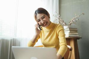 mulher asiática em roupas casuais é feliz e alegre enquanto se comunica com seu smartphone e trabalha em um café. foto