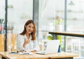 reunião on-line. jovem feliz usando computador portátil para conferência virtual, tendo chamada de vídeo em casa. alegre mulher asiática se comunicando com colegas, amigos remotamente. foto