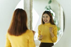 uma jovem asiática fala consigo mesma através de um espelho para construir sua autoconfiança e se fortalecer. foto