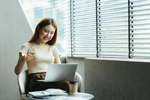 mulher asiática tendo chamada de vídeo em seu computador em casa. garota sorridente estudando online com o professor. foto