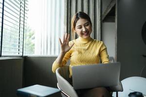 mulher asiática tendo chamada de vídeo em seu computador em casa. garota sorridente estudando online com o professor. foto