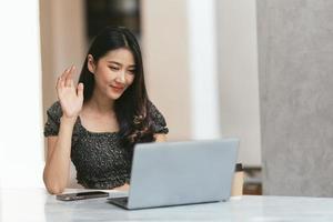 reunião on-line. jovem feliz usando computador portátil para conferência virtual, tendo chamada de vídeo em casa. alegre mulher asiática se comunicando com colegas, amigos remotamente. foto