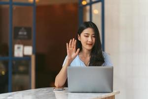 reunião on-line. jovem feliz usando computador portátil para conferência virtual, tendo chamada de vídeo em casa. alegre mulher asiática se comunicando com colegas, amigos remotamente. foto