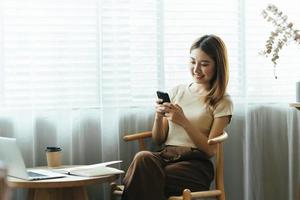 mulher asiática em roupas casuais é feliz e alegre enquanto se comunica com seu smartphone e trabalha em um café. foto