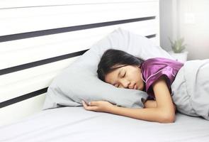 menina asiática dormindo durante a doença - ela tem um rosto pálido dorme na cama e cobertor. saúde ruim precisa de descanso.