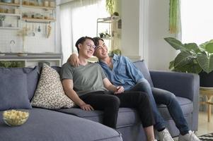 jovem casal gay sorridente assistindo tv na sala de estar em casa, lgbtq e diversidade foto