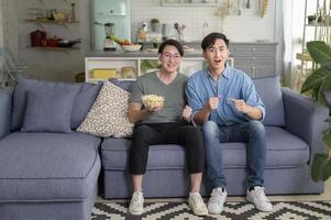 jovem casal gay sorridente assistindo tv na sala de estar em casa, lgbtq e diversidade foto