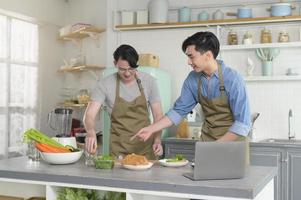 jovem casal gay sorridente cozinhando juntos na cozinha em casa, lgbtq e conceito de diversidade. foto