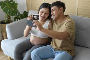 jovem grávida com marido abraçando e videochamada com familiares e amigos por smartphone nas mídias sociais, conceito de cuidados com a família e a gravidez foto