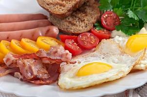 café da manhã inglês - ovos fritos, bacon, salsichas e pão de centeio torrado foto
