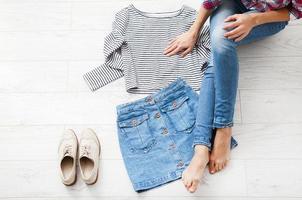 roupa casual de verão com diferentes acessórios e pernas femininas em jeans no piso de madeira branco. vista superior e copie o espaço. foto