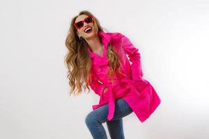 Feche a garota feliz em óculos de sol vermelhos e casaco rosa isolado no fundo branco. jovem animado, chocado e surpreso, roupa da moda. conceito de moda e compras. Cabelo ondulado longo. foco seletivo foto
