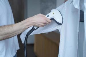 foto recortada de homem usando vaporizador de vestuário elétrico enquanto cozinhava enquanto camisa clássica em casa