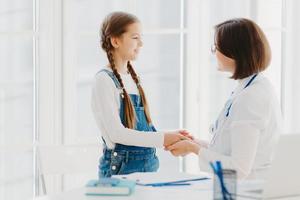 médica aperta a mão de paciente menina, fala palavras de apoio, se preocupa com a criança durante a consulta profissional, pronta sempre para ajudar com um bom tratamento. conceito de seguro médico foto