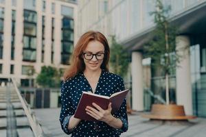 tiro ao ar livre de mulher ruiva faz anotações no bloco de notas faz planejamentos para o dia de trabalho foto