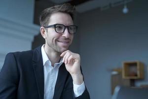 bonito empresário austríaco positivo usando óculos trabalhando remotamente em casa foto