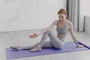 garota desportiva magro está esticando na esteira. aulas de ginástica em casa. reabilitação desportiva e saúde. foto