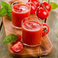 suco de tomate e tomates maduros em uma mesa de madeira foto