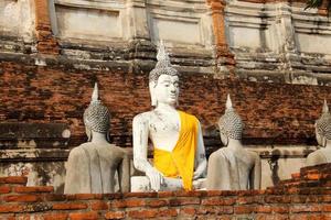 estátua de buda pintada de branco coberta de pano amarelo com parede de tijolo vermelho quebrada na frente e fundo no templo, província de ayutthaya, tailândia. foto