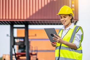 mulher de carga de contêiner de engenheira profissional em capacetes sorriu feliz depois de usar com sucesso o tablet para inspecionar o estoque de produtos de exportação e informações em seu negócio foto