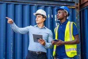 gerente do porto e um colega rastreando o inventário enquanto estão de pé para posicionar a caixa de contêineres de carga do navio de carga no transporte de contêineres de carga em uma grande doca comercial foto