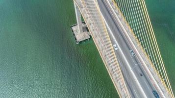 vista aérea do carro dirigindo em uma ponte com árvores da floresta natural, areia, praia tropical e ondas rolando na costa. foto