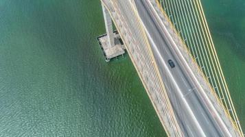 vista aérea do carro dirigindo em uma ponte com árvores da floresta natural, areia, praia tropical e ondas rolando na costa. foto