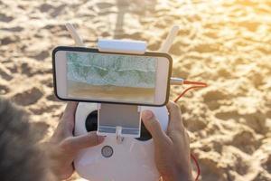 close-up das mãos do homem segurando o controlador para um drone com telefone. foto recortada de mãos de jovem segurando o controle remoto de um drone voador na praia