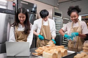 três jovens amigos e parceiros de inicialização de massa de pão e alimentos de confeitaria ocupados com trabalhos de panificação caseiros enquanto preparam pedidos on-line, embalam e entregam na padaria, pequeno empresário foto