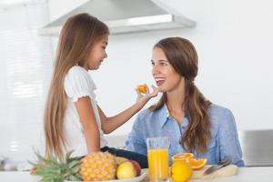 menina dando um segmento laranja para sua mãe