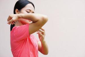 mulher coçando o braço de coceira no fundo cinza claro. causa de coceira na pele incluem picadas de insetos conceito de cuidados de saúde da pele. foto