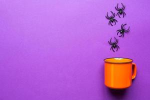 caneca laranja em um fundo roxo com aranhas. o conceito do feriado de halloween. cenário terrível, bebida terrível, diversão. copie o espaço, simular, categoricamente foto