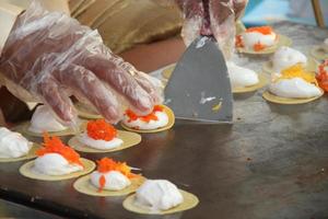 as mãos estão dobrando o crepe crocante tailandês na chapa quente. topo de crepe crocante são creme branco e coco salgado, tailândia. foto