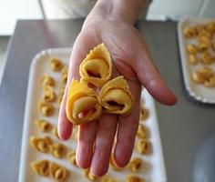 cozinheira italiana tem três massas tortellini cruas na mão.