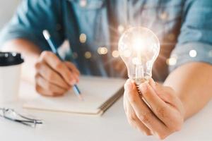 inovação através de ideias e ideias de inspiração. mão humana segurando a lâmpada para iluminar, ideia de criatividade e conceito de inspiração de desenvolvimento de negócios sustentáveis. foto