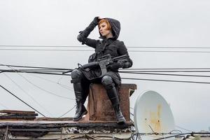jovem mulher no estilo techwear preto moderno com rifle posando no telhado, retrato de mulher ruiva cyperpunk ou conceito pós-apocalíptico