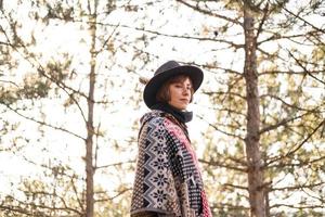 jovem viajante de mulher hipster de chapéu e poncho caminhando ao ar livre foto