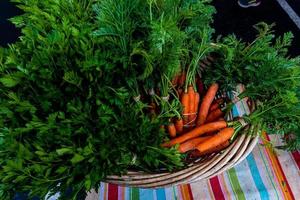 cesta tecida de cenouras laranja com topos de folhas verdes foto