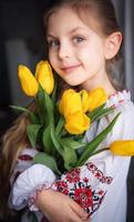 uma garotinha ucraniana em roupas tradicionais tem tulipas amarelas nas mãos