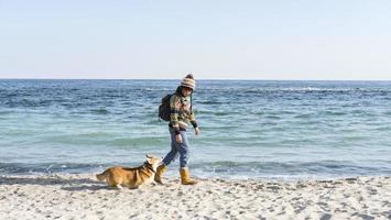 jovem fêmea feliz anda com cachorro corgi fofo na praia ensolarada de outono foto