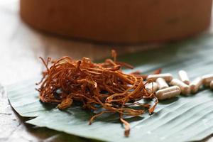 seco cordyceps militaris em uma folha de bananeira verde com fundo de madeira. cogumelo médico laranja para uma boa saúde com cápsulas. foto