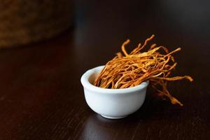 micélio seco cordyceps militaris em tigela branca com fundo de madeira. cogumelo médico laranja para uma boa saúde. foto