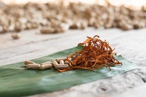 seco cordyceps militaris em uma folha de bananeira verde com fundo de madeira. cogumelo médico laranja para uma boa saúde com cápsulas. foto