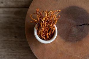 micélio seco cordyceps militaris em tigela branca com fundo de madeira. cogumelo médico laranja para uma boa saúde. foto