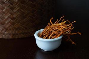 micélio seco cordyceps militaris em tigela branca com fundo de madeira. cogumelo médico laranja para uma boa saúde. foto