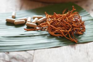 seco cordyceps militaris em uma folha de bananeira verde com fundo de madeira. cogumelo médico laranja para uma boa saúde com cápsulas. foto