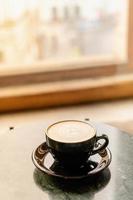 uma xícara de cappuccino com espuma em uma mesa de mármore perto da janela em um pequeno café aconchegante. bebida com leite vegetal, aveia, coco