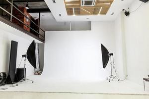 estúdio fotográfico vazio com equipamento de iluminação. interior do local de trabalho do fotógrafo com engrenagem profissional do conjunto de ferramentas. flash light cenas de fundo branco prontas para filmagem em estúdio. estúdio de fotógrafo moderno foto