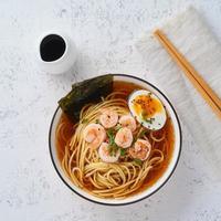 sopa asiática com macarrão, ramen com camarão. mesa de pedra branca, vista de cima foto